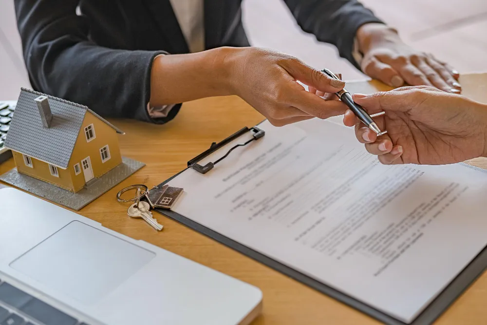 Mãos assinando contrato de imóvel, com chave e miniatura de casa, sobre como transferir imóvel para holding sem pagar ITBI.