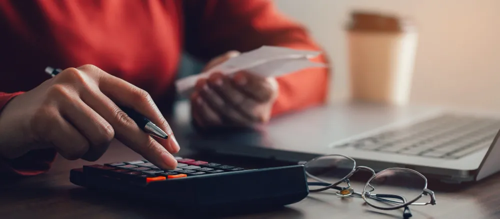 Mão com calculadora e papéis, imposto de renda sobre venda de imóvel na holding é menor?