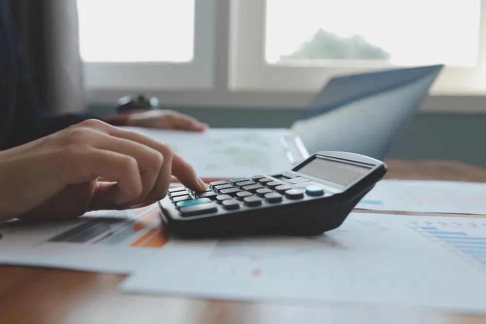 Mãos calculando, analisando dados e laptop, imposto de renda sobre venda de imóvel na holding é menor?