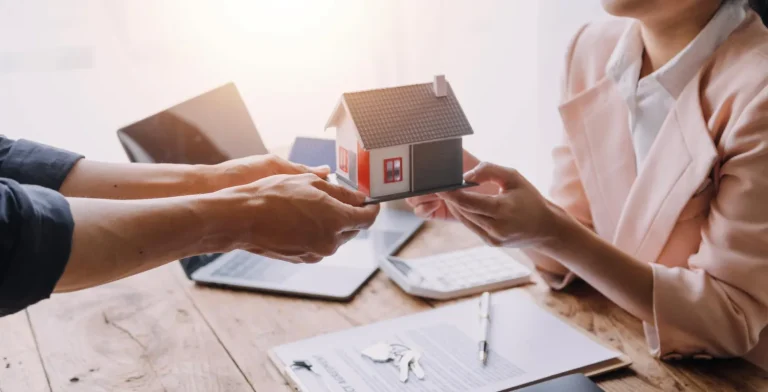 Duas pessoas trocam uma miniatura de casa, discutindo se bens colocados na holding familiar podem ser penhorados.