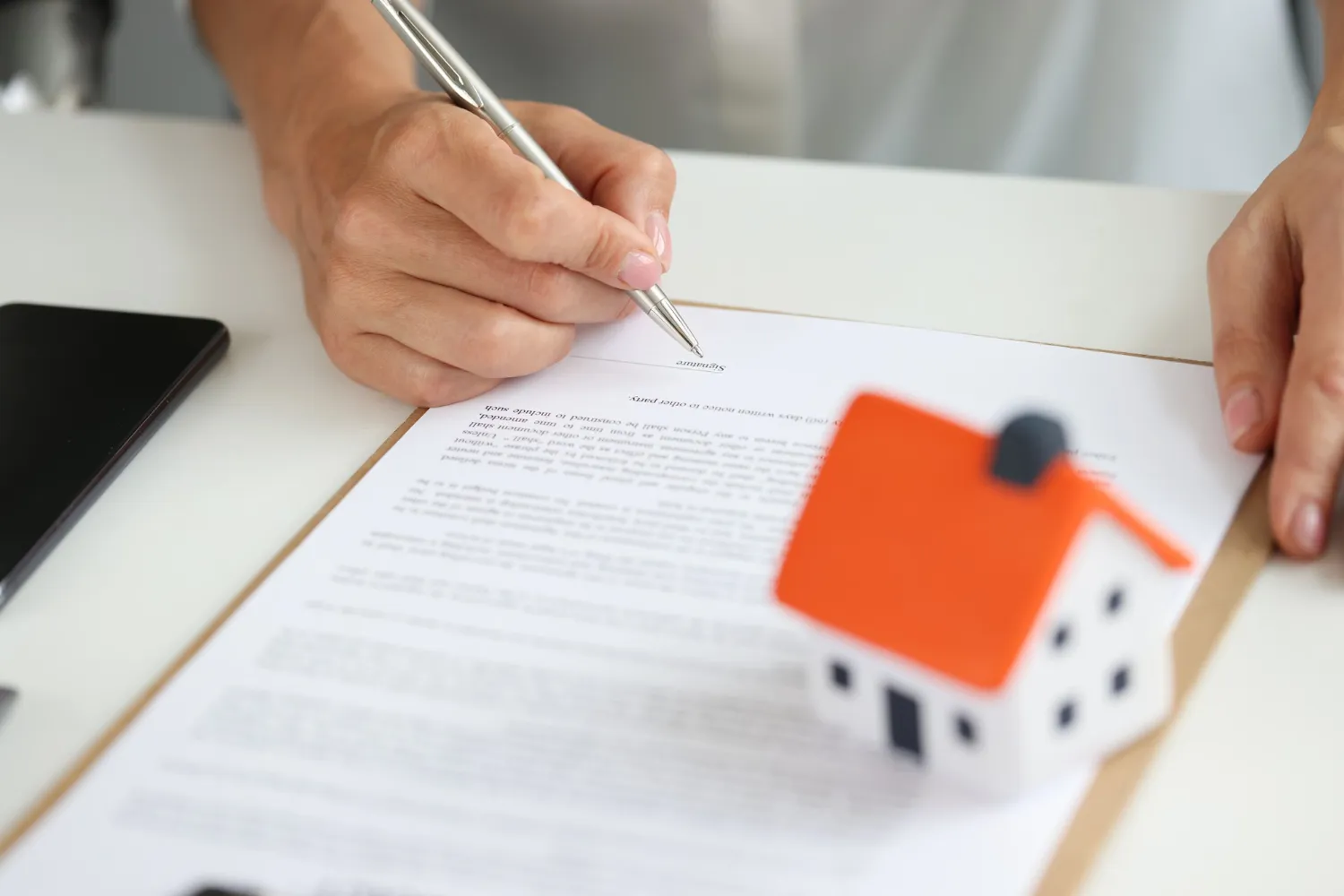 Mão assinando contrato com miniatura de casa, analisando vantagens e desvantagens da holding familiar.